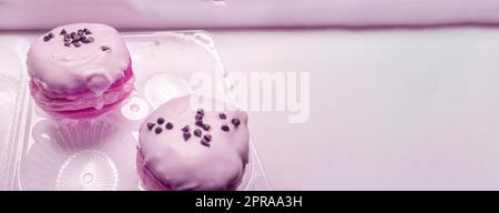 Two delicious donuts with icing sugar and chocolate chips in a transparent plastic container, a banner with a copy of the space on the right, pink tinting Stock Photo