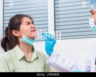 Doctor man take saliva sample through nose with cotton swab to check coronavirus test from Asian young woman Stock Photo