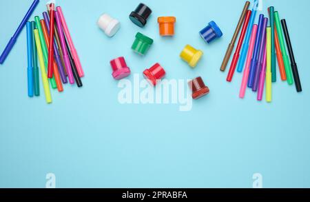 Multi-colored felt-tip pens and acrylic paint in a plastic jar on a blue background Stock Photo