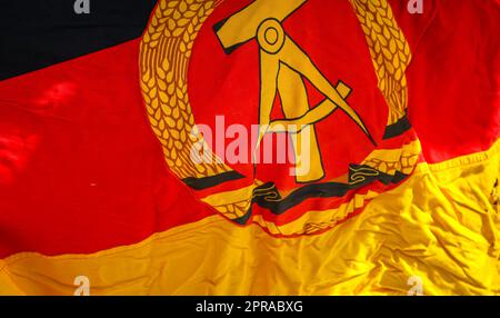 A piece of the flag of the former GDR with emblem, hammer, compass, ear wreath. Stock Photo