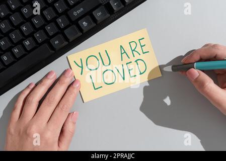 Hand writing sign You Are Loved. Internet Concept Somebody loves you have strong feelings happy excited Businesswoman Holding Note With Important Message On Office Desk. Stock Photo