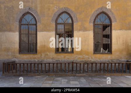 Wooden arched window with wrought iron grid over yellow stone bricks wall and wooden balustrade Stock Photo