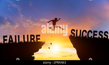 Silhouette man jumping from FAILURE to SUCCESS wording on cliffs with cloud sky and sunrise. Successful achievement Concept. Stock Photo