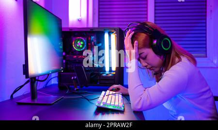 Angry Asian gamer wearing gaming headphones playing joystick console video game Stock Photo