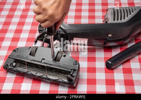Repair of household appliances. Professional technician repairs a vacuum cleaner. Household appliances customer service. Battery hoover. Repair by a specialist on site. Stock Photo