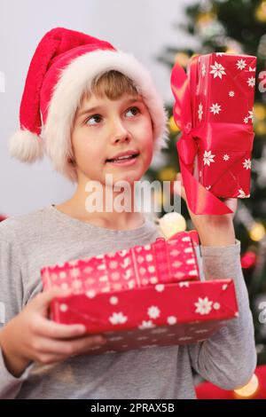 Portrait of a curious child holding presents by the Christmas tree on Christmas morning. Stock Photo