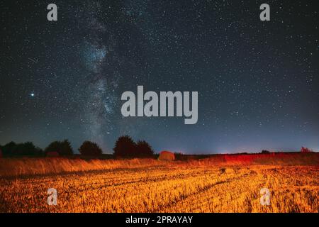 Milky Way Galaxy In Night Starry Sky Above Haystack In Summer Agricultural Field. Night Stars Above Rural Landscape With Hay Bale After Harvest. Agricultural Concept Stock Photo