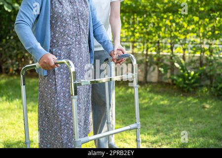 Caregiver help and care Asian senior or elderly old lady woman use walker with strong health while walking at park in happy fresh holiday. Stock Photo