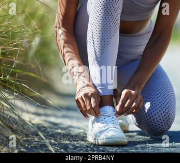 Readying herself for a serious run out in nature. Closeup shot of an unrecognisable woman tying her shoelaces while exercising outdoors. Stock Photo