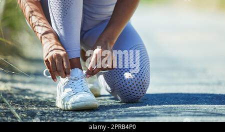 Gearing up to tackle a tough path. Closeup shot of an unrecognisable woman tying her shoelaces while exercising outdoors. Stock Photo