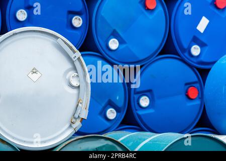 Old chemical barrels. Blue and green oil drum. Steel and plastic oil tank. Toxic waste warehouse. Hazard chemical barrel with warning label. Industrial waste in drum. Hazard waste storage in factory. Stock Photo