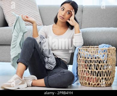 Where does all this laundry even come from. a young woman doing the laundry at home. Stock Photo