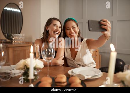 Its a bestie selfie only. two young friends sitting together and using a cellphone to take selfies during a New Years dinner party. Stock Photo