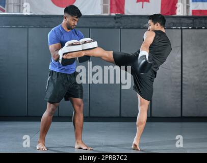 Active, athletes and fit men kick boxing and doing sport training workout in a gym. Two male partners or MMA boxer and trainer practice sparring exercises for a healthy wellness lifestyle. Stock Photo
