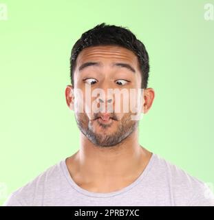 Can you do this. a handsome young man making a face against a green background in studio. Stock Photo
