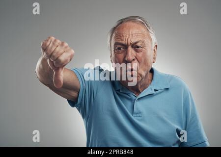 No I dont like that at all. a unhappy older man giving the thumbs down in a studio against a grey background. Stock Photo