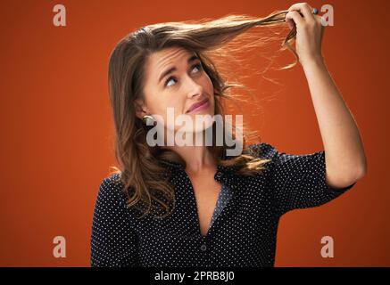 Are those split ends. an attractive young woman standing alone against a red background in the studio and touching her hair. Stock Photo