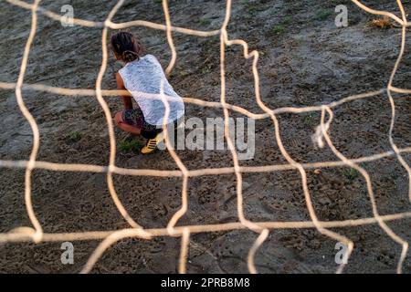 A young Colombian female football player sits inside the goal during a training session on a dirt playing field in Necoclí, Antioquia, Colombia. Stock Photo