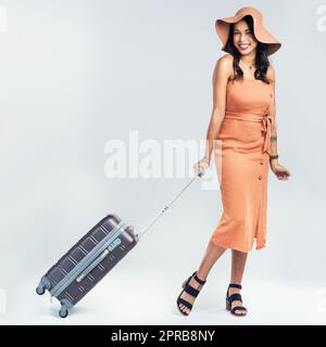 I have a desire to travel the world. Studio shot of a woman pulling her suitcase against a white background. Stock Photo