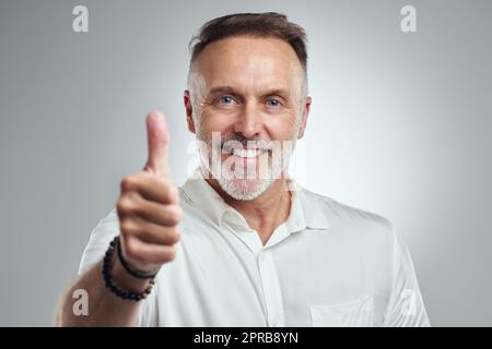 You did so well. Studio portrait of a mature man showing thumbs up against a grey background. Stock Photo