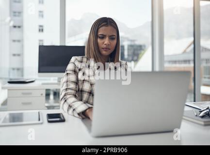 Something doesnt seem quite right. an attractive young businesswoman sitting alone in her office and looking confused while using her laptop. Stock Photo