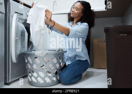 This washing powder really makes clothes sparkle. a young woman preparing to wash a load of laundry at home. Stock Photo