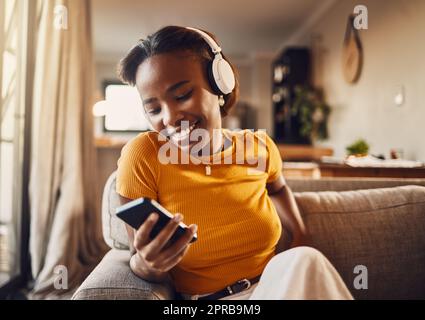 Young woman texting, browsing and scrolling social media on a phone feeling happy, carefree and smiling. Listening to music, podcast or watching funny internet memes online while relaxing on a sofa Stock Photo