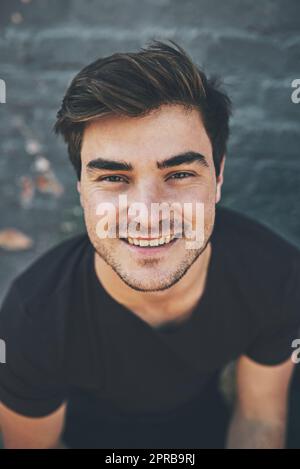 Laughing, happy and smiling face of a student isolated against a grey city wall outside. Portrait and headshot of a stylish, cool and funky young man enjoying a weekend break alone in town Stock Photo