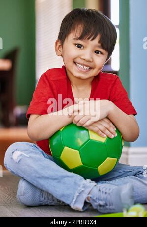 Wanna go outside and kick the ball with me. Portrait of an adorable little boy playing with a soccer ball at home. Stock Photo