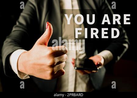 Hand writing sign You Are Fired. Conceptual photo Getting out from the job and become jobless not end the career Businesswoman Holding Cellphone In One Hand And Showing Thumbs Up. Stock Photo