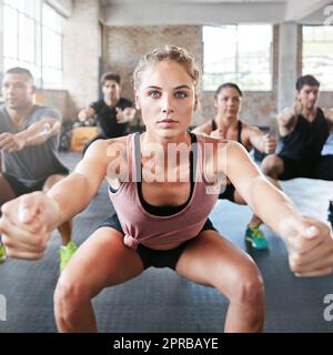 Getting focused on her fitness. a group of people doing squats in a gym. Stock Photo