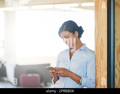 Focused on her schedule. a young woman using her cellphone while standing in an office. Stock Photo