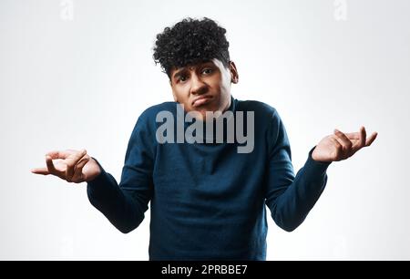 If youre looking for answers, I dont have any. Studio shot of a young man shrugging his shoulders against a grey background. Stock Photo