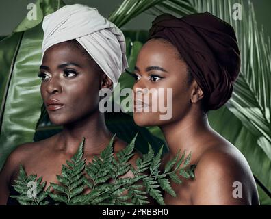 Staying true to natural beauty. Studio shot of two beautiful young women posing in front of palm leaves against a grey background. Stock Photo