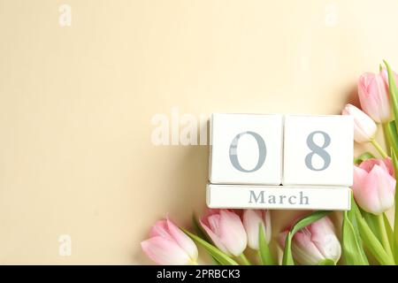 Wooden block calendar with date 8th of March and tulips on beige background, flat lay. Space for text Stock Photo