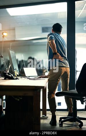 Putting his health at risk for the sake of business. Rearview shot of a businessman suffering from backache while working at night. Stock Photo