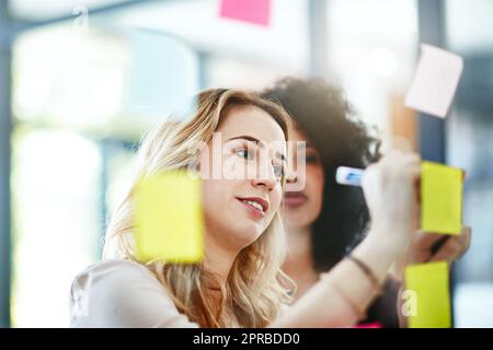 Manager brainstorming, planning and writing sticky notes on glass window. Female worker showing corporate leadership, and management skills. Detail information on tasks to meet company objectives Stock Photo