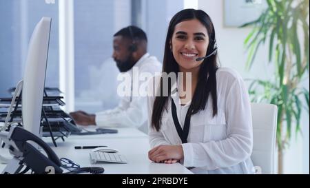 Its always a pleasure to help our clients further. Portrait of a young businesswoman working on a computer in a call centre with a colleague in the background. Stock Photo