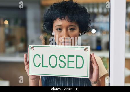Weve had to close our doors. Portrait of a young woman holding a closed sign in her store. Stock Photo