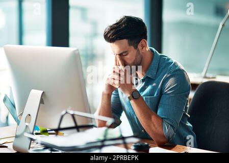 Businessman suffering from a headache or migraine due to stress caused by deadlines and work pressures. Professional in pain feeling anxious, overwhelmed and stressed while busy on his computer desk Stock Photo