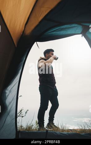 Nature is a lot cheaper than therapy. a young man drinking coffee while camping in the wilderness. Stock Photo