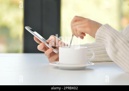 Closeup shot of an unrecognizable woman having a cup of coffee at a cafe and using a phone Stock Photo