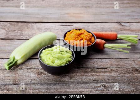 Tasty puree in bowls, zucchini and carrots on wooden table Stock Photo