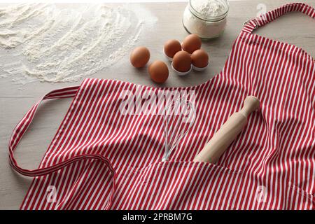 Red striped apron with kitchen tools and different ingredients on wooden table Stock Photo
