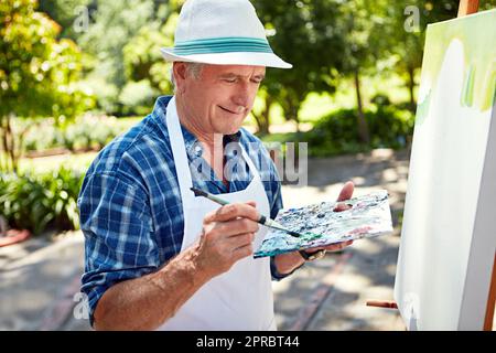For him, happiness is painting. a senior man painting in the park. Stock Photo
