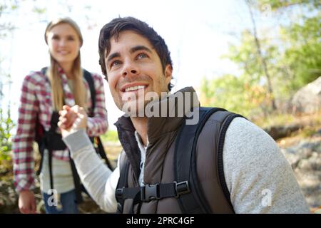 Leading her down safely. A handsome young hiker helping his girlfriend as they hike down a mountainside. Stock Photo