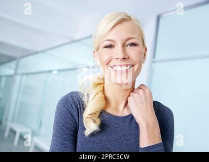 Portrait of an attractive young blonde woman standing in an office. One cheerful female businessperson at work. Business professional smiling while Stock Photo
