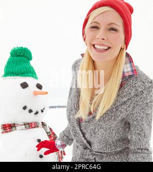 Her boyfriend was regretting not wearing his coat. a beautiful young woman standing beside a snowman. Stock Photo
