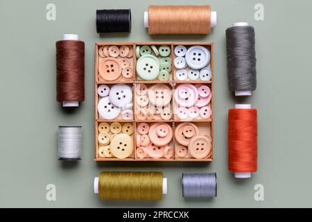 Composition with box of different buttons and thread spools on grey background Stock Photo