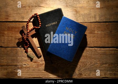 Holy Bibles with prayer beads and cross on wooden background Stock Photo